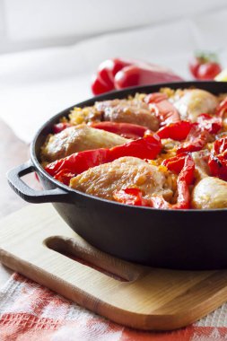 Pirinç ve dökme demir güveç içinde kırmızı dolmalık biber bir yatak üzerinde pişmiş tavuk uyluk ve bacaklar