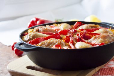 Pirinç ve dökme demir güveç içinde kırmızı dolmalık biber bir yatak üzerinde pişmiş tavuk uyluk ve bacaklar