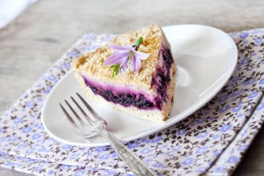 Mor bir çiçek ile süslenmiş bir tabakta yaban mersinli kek parçası