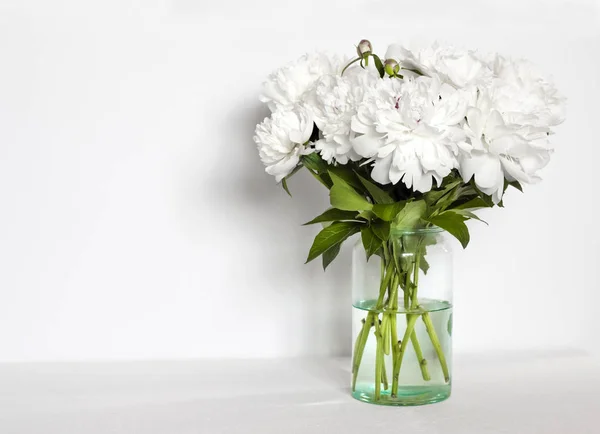 Bouquet de pivoines blanches dans un vase en verre sur fond de mur blanc — Photo