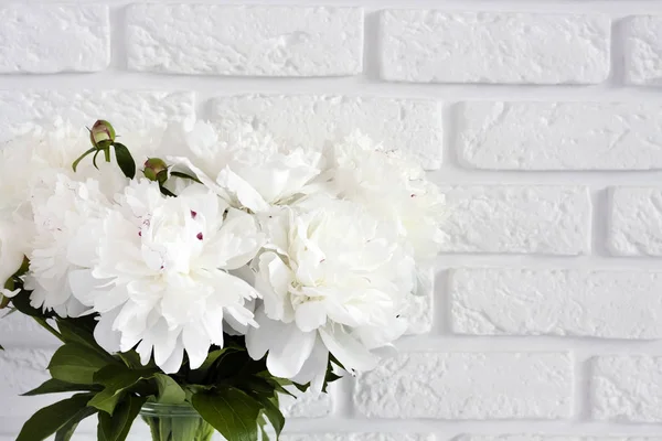Bouquet of white peonies in a glass vase on a white break wall — Stock Photo, Image
