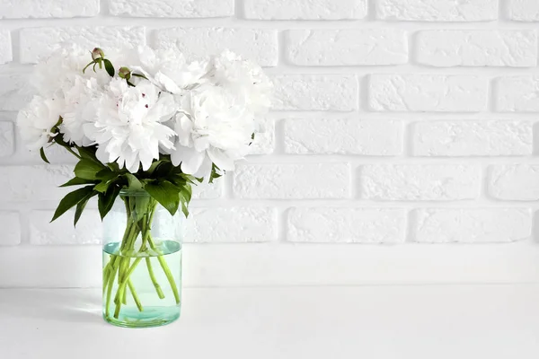 Bouquet of white peonies in a glass vase on a white break wall background with copy space — Stock Photo, Image