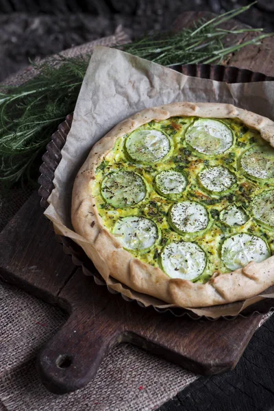 Homemade courgette and goat cheese pie on a dark rustic wooden board background — Stock Photo, Image