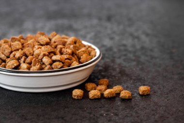 Siyah zemin üzerinde beyaz seramik bir kasede fotokopi alanı olan kuru hayvan mamaları.