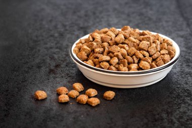 Siyah zemin üzerinde beyaz seramik bir kasede fotokopi alanı olan kuru hayvan mamaları.