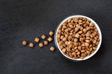 Siyah arka planda beyaz bir seramik kasede kurutulmuş evcil hayvan yiyeceği. Düz konum, üst görünüm, kopyalama alanı