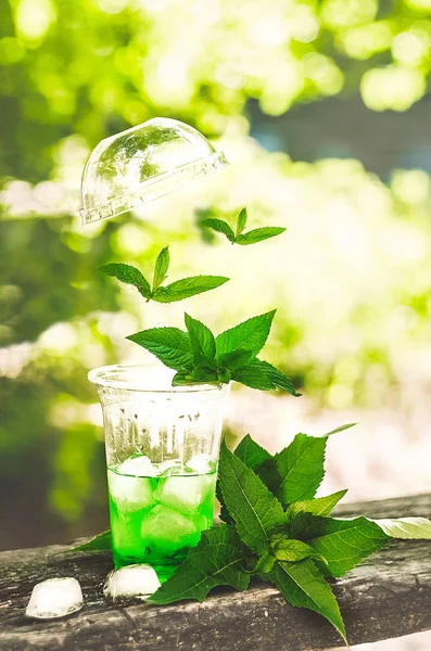 flying cap with a cocktail. levitation. mint falls into the drink. ice cubes and juice. nature. summer drink