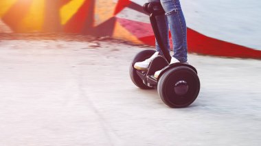 Kız jiroskopun üzerinde duruyor. Tekerlekler gider. Güneşli bir gün.