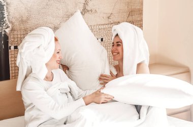 Anne ve kızı yatakta birlikte oynuyorlar. Dövüş yastıkları. eğlenceli.