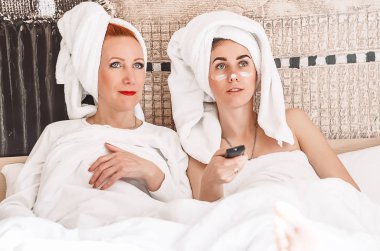 Anne ve kızı yatağa uzanıp televizyon izliyorlar. Havluya sarılıp yıkandıktan sonra..