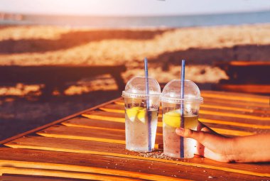 Deniz kenarında ferahlatıcı kokteyller. Kadehler içinde saman ve limon. El onları tutar.