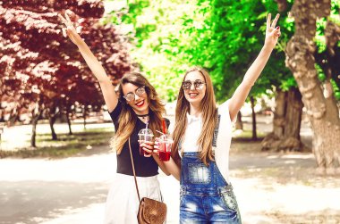Neşeli arkadaşlar barış jesti gösterir. Yüzüne gülümse. Pipet ve buzlu kokteyller. İletişim ve yürüyüş. Yaz. bir park