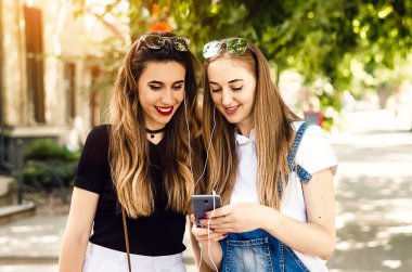 Kız arkadaşlar kulaklıkla dinlemek için telefondaki müziği seçerler. Sokak yürüyüşü