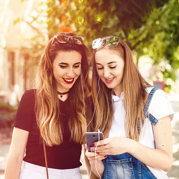 İki kız sokakta yürüyorlar ve telefona bakıyorlar. teknoloji ve insanlar