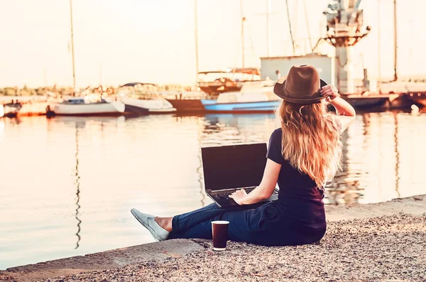 morning sunrise near the sea girl sitting and looking at the landscape. freelancer. hat on the head. a glass of hot coffee. a laptop