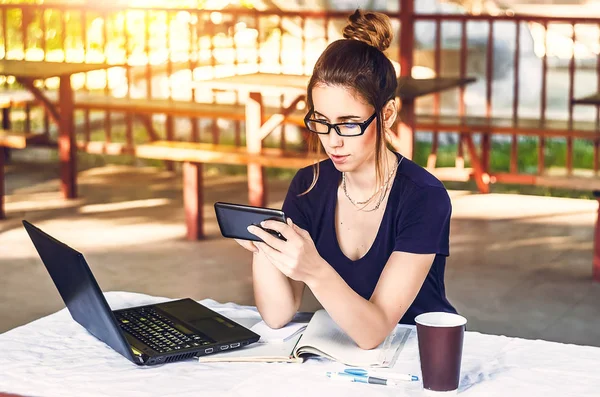 Kız şu anda telefona bakıyor. Temiz hava. Masada bir dizüstü bilgisayar var. içki bardağı. Bağımsız, iletişim, seyahat.