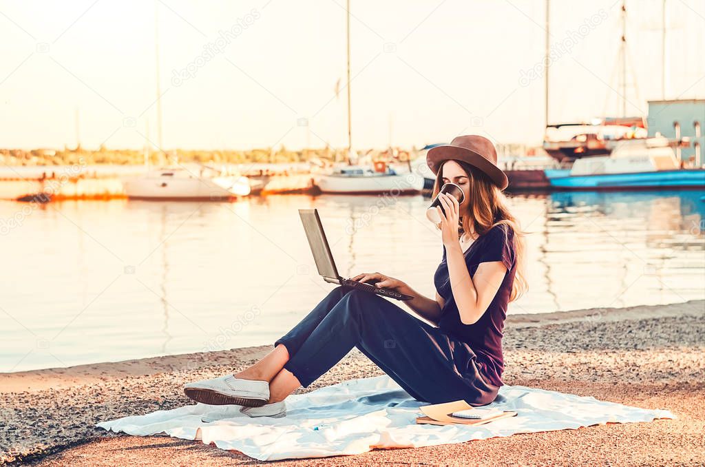 the girl drinks hot coffee at work. beautiful view of the sea and yachts. dawn. Sun rays. wireless internet. a laptop