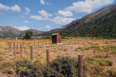 Dağların eteklerinde, güneşli yaz havasında, kırsal alanda, doğada bulunan ahşap kahverengi tuvalet kabini.