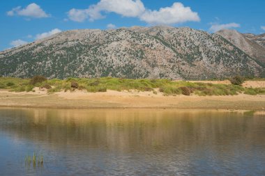 Batı adasındaki Omalos köyündeki Girit Dağı manzarası. Dağlar güneşli gökyüzünün altındaki küçük bir göle güzelce yansıyor.