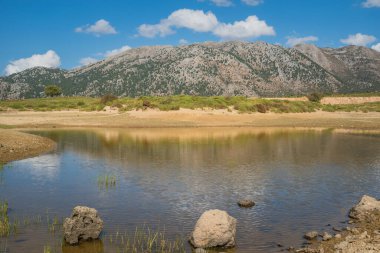 Batı adasındaki Omalos köyündeki Girit Dağı manzarası. Dağlar güneşli gökyüzünün altındaki küçük bir göle güzelce yansıyor.