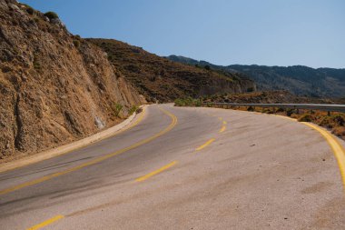 Güneşli bir günde, Beyaz Dağlar 'daki Omalos köyünün yakınındaki Girit adasındaki bir dağın etrafından dolanan yol bölümü.