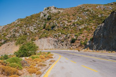 Güneşli bir günde, Beyaz Dağlar 'daki Omalos köyünün yakınındaki Girit adasındaki bir dağın etrafından dolanan yol bölümü.
