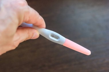 Elinde kahverengi arka plan üzerinde negatif hamilelik testi var.