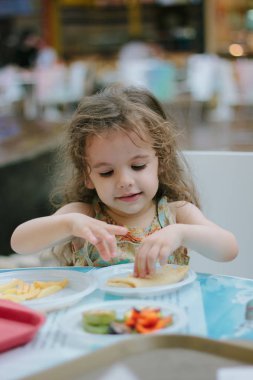Küçük kız kafede ya da restoranda yemekle eğleniyor.