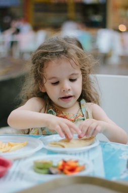 Küçük kız kafede ya da restoranda yemekle eğleniyor.
