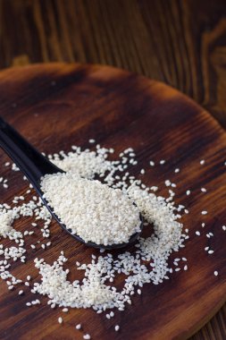 Tahta arka planda siyah kaşıkta beyaz susam tohumları.