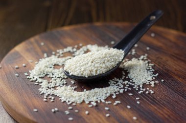 Tahta arka planda siyah kaşıkta beyaz susam tohumları.