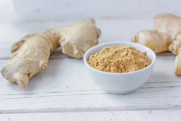 Grounded ginger and ginger root on white wooden surface.