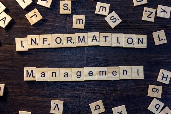 information management word made with scrabble letters on a black wooden table.