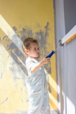 Küçük kız duvarları boya rulosuyla boyuyor.