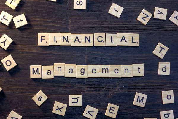 financial management word made with scrabble letters on a black wooden table.