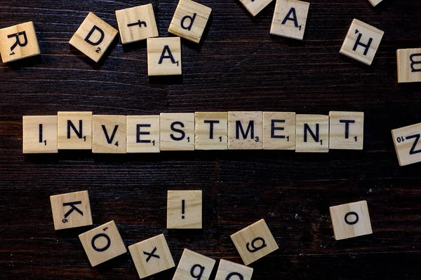 Investment word made with scrabble letters on a black wooden table.