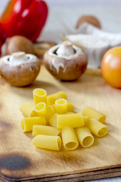 Pasta seca de rigatoni sobre tabla de cocina de madera con verduras. —  Fotos de Stock