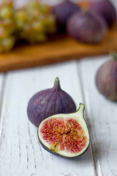 Metà del fico sul tavolo di legno bianco con altri fichi e frutti . — Foto Stock