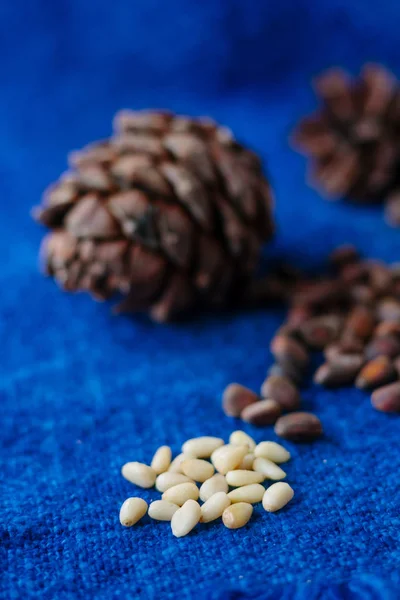 peeled cedar or pine nuts with pine cone on blue surface.
