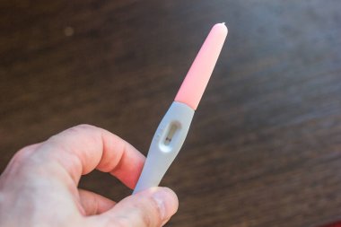 Elinde kahverengi arka plan üzerinde negatif hamilelik testi var..