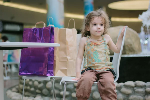 Niña cansada de ir de compras y sentada con las bolsas de compras. — Foto de Stock
