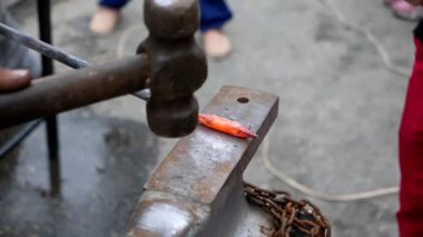 İki demirci örs üzerinde metal bir detay dövüyor. 