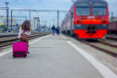 Küçük kız eğitime gidiyor. Tren istasyonunda çantasıyla gezecek.