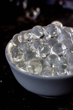 Siyah arka planda beyaz kasede hidrojel toplar..