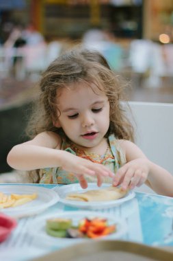 Küçük kız kafede ya da restoranda yemekle eğleniyor.
