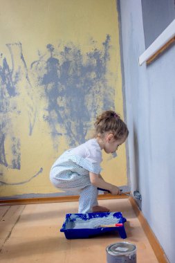 Küçük kız duvarları boya rulosuyla boyuyor.