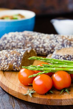 Taze ve olgun kuşkonmaz ve ahşap tahtada ekmekli kiraz domatesleri.