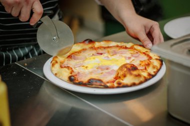 Şef pizzayı yuvarlak pizza bıçağıyla keser.
