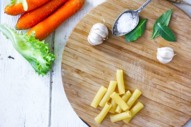 Kuru rigatoni makarna ve ahşap tahtanın üzerine biraz sebze.