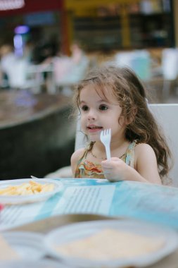 Kafede ya da restoranda elinde plastik çatal olan küçük bir kız..